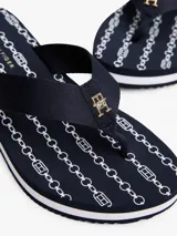 Ojotas de cuña de altura media, color azul marino, con tiras anchas de tejido trenzado y una pequeña insignia dorada con el monograma TH en la tira del dedo. La plataforma tiene un diseño de rayas blancas y un patrón de cadenas blancas.