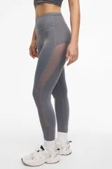 Calza deportiva larga color gris, con cintura alta, detalles de transparencias laterales en tul y bolsillos laterales.