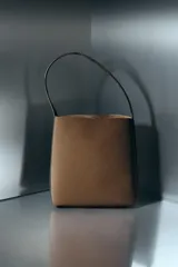 Bolso de hombro tipo saca, de diseño minimalista y estructura flexible. Cuenta con asa de hombro, cierre mediante clip metálico y compartimento interior extraíble con cremallera.