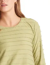 Blusa de silueta fluida en tejido shaggy con textura de franjas horizontales. Presenta cuello a la base, mangas tres cuartos con tajo lateral en el puño y ruedo redondeado con corte asimétrico, siendo más largo en la parte posterior.