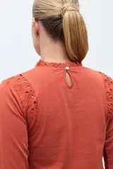 Remera de manga larga color terracota, con cuello alto y detalles de broderie en los hombros y puños acampanados.