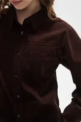 Camisa de pana color marrón, con cuello camisero, cierre frontal de botones y bolsillos en el pecho. Presenta un corte entallado y mangas largas.