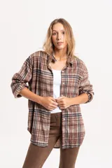Camisa de corte oversize con estampado de cuadros en tonos marrones y beige. Presenta cuello clásico, cierre frontal con botones y mangas largas con puños simples.