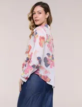 Camisa de gasa blanca con estampado floral multicolor, cuello con solapa, mangas largas y cierre frontal con botones. Cuenta con terminación delantera anudada y espalda más larga.
