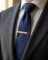 Clip de corbata metálico en tono dorado con diseño minimalista de líneas grabadas.