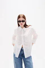Camisa de algodón blanca, de corte clásico con cuello camisero, cierre frontal con botones, mangas largas con puños y bolsillo frontal en el pecho.