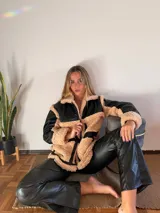 Campera color beige con detalles en negro de piel sintética con cuello y solapas amplias, cierre frontal con cremallera y bolsillos laterales.