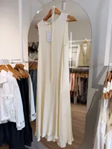 Vestido largo sin mangas en tono natural, confeccionado en tela texturada con relieve, de corte fluido, con bolsillos laterales y un cordón fino para anudar en la cintura.