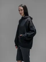 Hoodie oversize color negro, confeccionado en frisa gamuzada de algodón con recortes en hombros y bolsillo frontal tipo cargo con solapa en material técnico. Presenta capucha forrada y puños y ruedo acanalados.