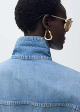 Chaqueta de jean con diseño oversize, cuello camisero, cierre frontal con botones metálicos, dos bolsillos de parche con solapa en el pecho y dos bolsillos laterales de ribete.