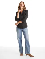 Camisa entallada de color negro con pechera estructurada mediante alforzas horizontales. Presenta cuello con solapa, escote en V, cierre frontal con botones y mangas tres cuartos con puños anchos rebatibles.