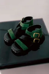 Sandalias con plataforma color verde y negro, con tiras de cuero y hebillas metálicas.