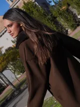 Buzo color crudo con cuello de piel sintética color crema, abertura parcial con cierre de cuero marrón y hebilla dorada, puños con ajuste de cuero marrón y bolsillos laterales.