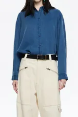 Camisa de manga larga color gris claro con efecto lavado, corte recto y botones frontales marrones. Presenta cuello camisero y pespuntes a contraste.