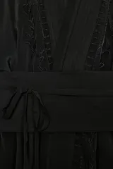Kimono largo de manga larga con diseño abierto, confeccionado en tejido satinado negro. Presenta detalles de bordados florales a tono en el frente y en los puños, e incluye un cinturón tipo fajín ajustable con lazadas en la cintura.