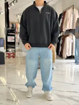 Buzo gris oscuro de corte oversize con cuello alto y cierre frontal parcial. Cuenta con mangas largas y puños elásticos, además de un pequeño bordado con texto en el pecho.