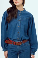 Camisa de denim azul oscuro con cuello mao, mangas abullonadas con puños elastizados y cierre frontal de botones metálicos.