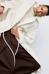 Trench oversize de cuello solapa y manga larga, con cintura ajustable mediante cordones y cierre frontal oculto. Cuenta con bolsillos laterales y forro interior.