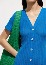 Vestido midi de crochet color azul, con escote en pico, manga corta y cierre frontal con botones blancos. Presenta un diseño recto y tejido de punto calado.