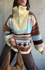 Sweater de tejido de punto con diseño a rayas horizontales y motivos geométricos, cuello alto con cierre frontal parcial, mangas largas abullonadas y puños acanalados.