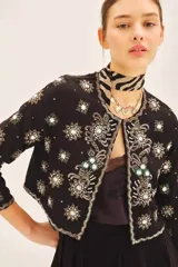 Saco corto de corte entallado con escote redondo, confeccionado en tejido negro con bordados artesanales de lentejuelas y pedrería en forma de estrellas y motivos florales en frente, espalda y mangas.