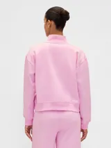 Buzo deportivo de color rosado con cuello alto y medio cierre frontal. Presenta el logo de la marca Gap 1969 bordado en el pecho junto a un emblema circular. Posee mangas largas con puños elásticos y un corte holgado.