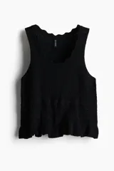 Musculosa corta negra de punto suave estilo crochet, sin mangas, con escote redondo pronunciado con ribete festoneado y bajo acanalado con volado.
