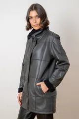 Campera de cuero color tostado con diseño de paneles, cuello alto y puños con forro de corderito sintético. Presenta cierre frontal con botones grandes y bolsillos laterales.