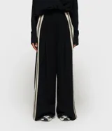 Pantalón ancho de corte oversize, color negro, con cintura alta ajustable con cordón. Presenta pliegues frontales profundos y cintas a rayas color beige/crema en las costuras laterales.