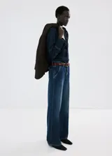 Jeans de tiro medio y corte wide leg, confeccionados en denim de algodón azul oscuro con lavado uniforme. Presentan cierre frontal con botón y cremallera, bolsillos laterales y traseros, y trabillas para cinturón.