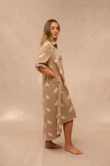 Vestido largo estilo camisero de color beige con estampado de plumas en tono más claro, cuello camisero, botonadura frontal completa, bolsillos laterales y mangas largas con presilla para arremangarlas.