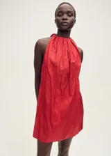 Vestido corto de cuello halter con diseño recto y fruncido en la parte superior. Presenta un cierre de lazo en la nuca y un acabado con textura sutil.