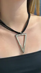 Gargantilla tipo choker con cordones negros múltiples y dije metálico plateado en forma de triángulo invertido.