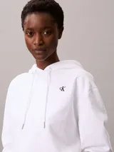 Buzo con capucha Calvin Klein de corte cropped, confeccionado en tejido de algodón y poliéster. Presenta un diseño minimalista en color blanco con el logotipo de la marca bordado en pequeño en el pecho y cordones ajustables en la capucha.