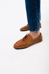 Mocasín de estilo relajado confeccionado en cuero gamuzado color tostado. Presenta detalles fruncidos en la puntera, cordones decorativos en el empeine y el logo de la marca grabado en el lateral.
