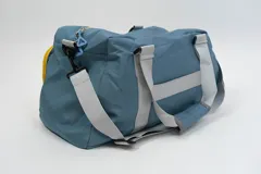 Bolso deportivo color rosa con detalles en beige y gris. Tiene doble asa de mano y correa de hombro ajustable. Cuenta con dos bolsillos frontales con cierre y logo de la marca en la esquina inferior derecha.