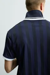Polo de corte relajado confeccionado en tejido técnico, con diseño de rayas verticales en tonos azul marino y negro. Presenta cuello solapa con abertura frontal y detalles de rib en contraste en cuello y mangas. Incluye estampado frontal con el número 98 y la inscripción France, además de una etiqueta aplicada en el ruedo inferior.