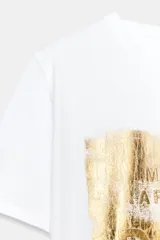 Camiseta de algodón de corte regular con cuello redondo y manga corta. Presenta un estampado frontal metalizado en tono dorado con diseño gráfico.