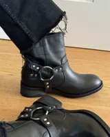 Botín de cuero vacuno color negro, con diseño estilo biker. Presenta correas ajustables con hebillas metálicas y una argolla lateral decorativa. Cuenta con suela de goma y tacón bajo.