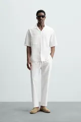 Pantalón de corte relajado color beige confeccionado en tejido de mezcla de algodón y lino. Posee cintura elástica ajustable con cordón, bolsillos frontales y bolsillos traseros de vivo.