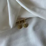 Aros colgantes dorados con forma de argolla con textura, de los que cuelga un dije circular con forma de rosa de los vientos con incrustaciones de strass.
