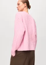 Jersey de punto trenzado color rosado, con cuello redondo y mangas largas de corte recto.