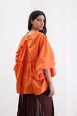 Camisa holgada de popelina de algodón con rayas verticales en tonos rosado, gris y blanco. Presenta cuello alto con volado, hombros caídos, mangas anchas abullonadas y cierre frontal con botones.