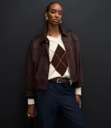 Campera bomber de gamuza sintética color marrón oscuro, con cuello clásico, cierre frontal, hombros caídos y puños ajustados. Presenta un diseño holgado con textura aterciopelada.