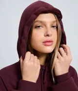 Buzo tipo hoodie color bordó, con corte oversized, capucha ajustable con cordones y bolsillo canguro delantero. Presenta un estampado gráfico pequeño en el pecho con tipografía estilo college.