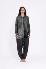 Camisa de calce relajado, color gris con efecto degradé o teñido, con cuello clásico y cierre frontal de botones. Presenta bolsillos grandes y caídos en la parte inferior del frente.