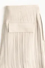 Pantalón tobillero de tiro alto en tejido arrugado color beige, con cierre de botón, bolsillos laterales y bajo ajustable con cordón.