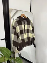 Sweater de punto con diseño de cuadros grandes en color marrón y crema, cuello tipo polo y cierre frontal con botones.