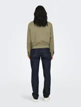 Campera corta color verde militar, de manga larga, con cuello redondo y cierre frontal de botones. Presenta dos bolsillos delanteros con solapa y elástico en la cintura.