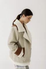 Gamulán de paño en color beige jaspeado con detalles en cuero sintético marrón y forro de corderito sintético blanco. Presenta cierre frontal cruzado, cuello solapa, bolsillos laterales y puños con vuelta.